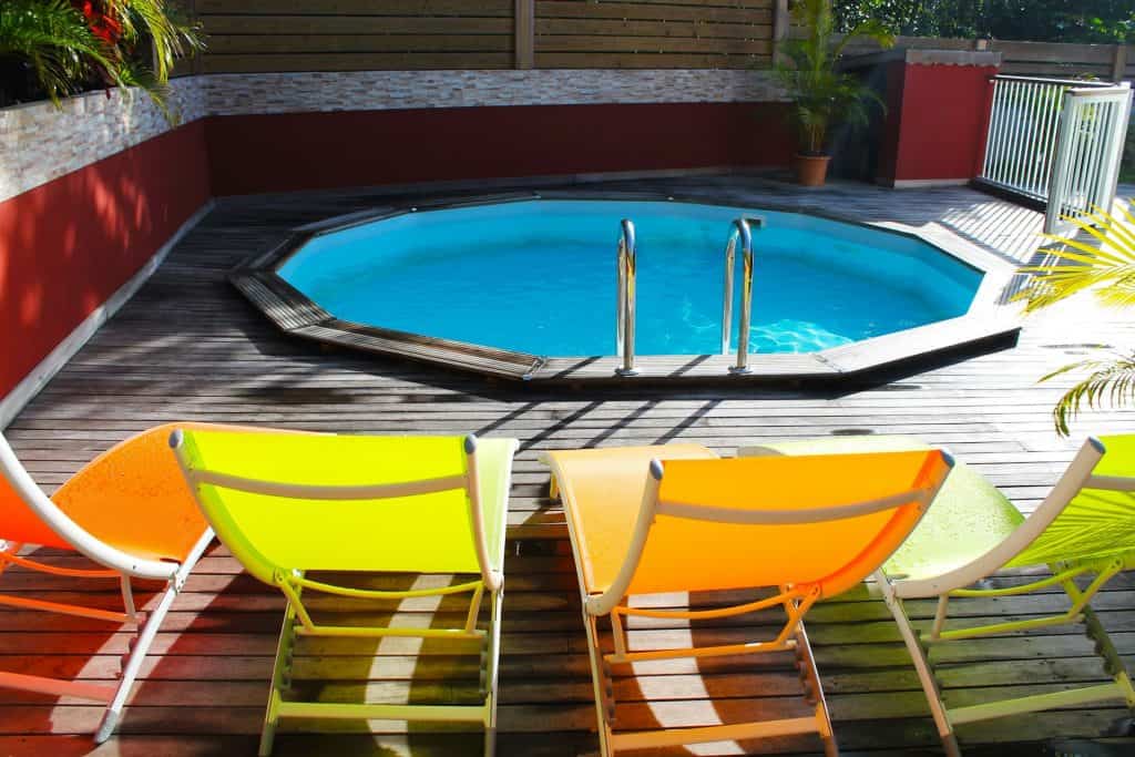 A beautiful private backyard pool with vibrant, colorful lounge chairs on a wooden deck, surrounded by lush greenery and privacy fencing, perfect for relaxing and enjoying summer days.