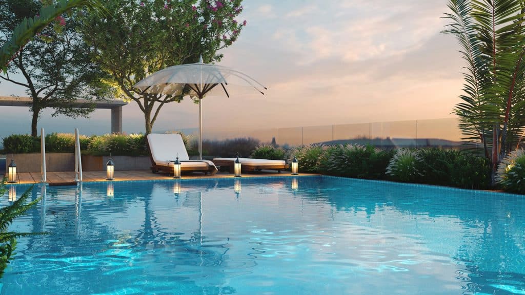 Beautiful backyard pool at sunset with lounge chairs, umbrella, and lush greenery, illustrating the serene setting for choosing between saltwater and chlorine pool systems.