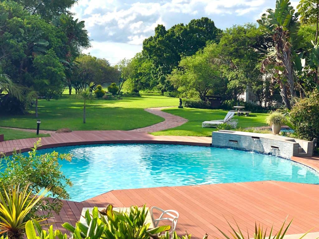 Beautiful backyard pool with lush greenery and a wooden deck, illustrating careful planning to avoid costly change orders in pool projects.