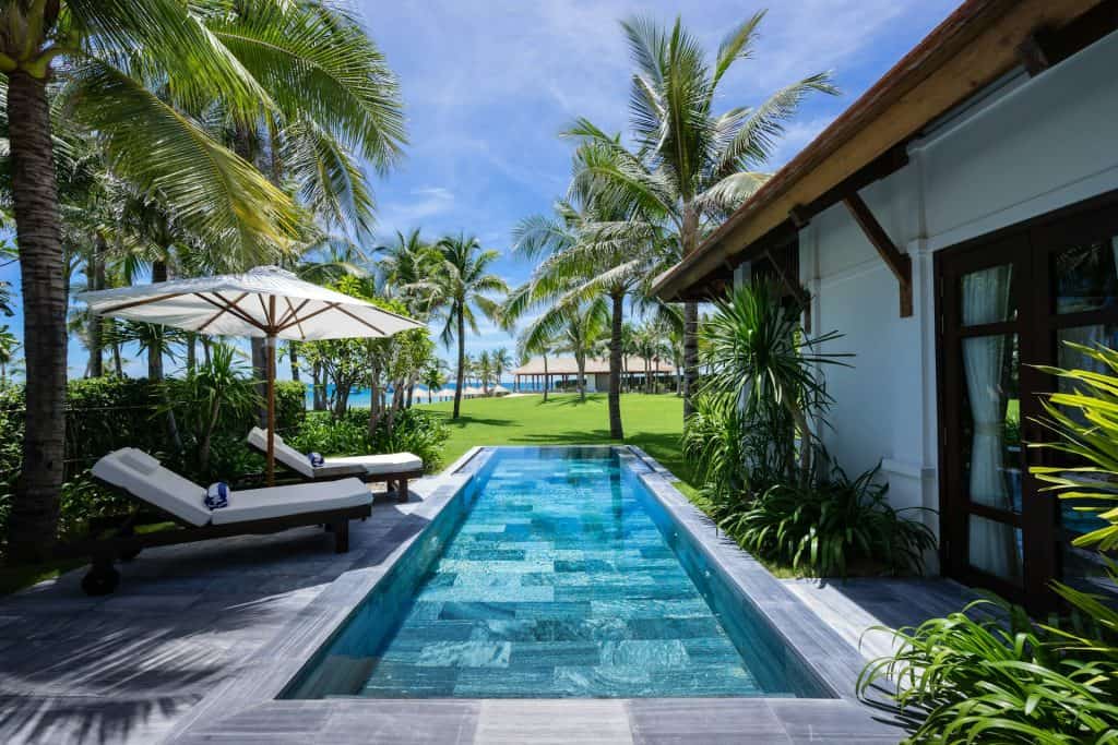 Beautiful in-ground pool with tropical landscaping, lounge chairs, and a shaded umbrella, perfect for relaxing and enjoying outdoor living in a tropical setting.