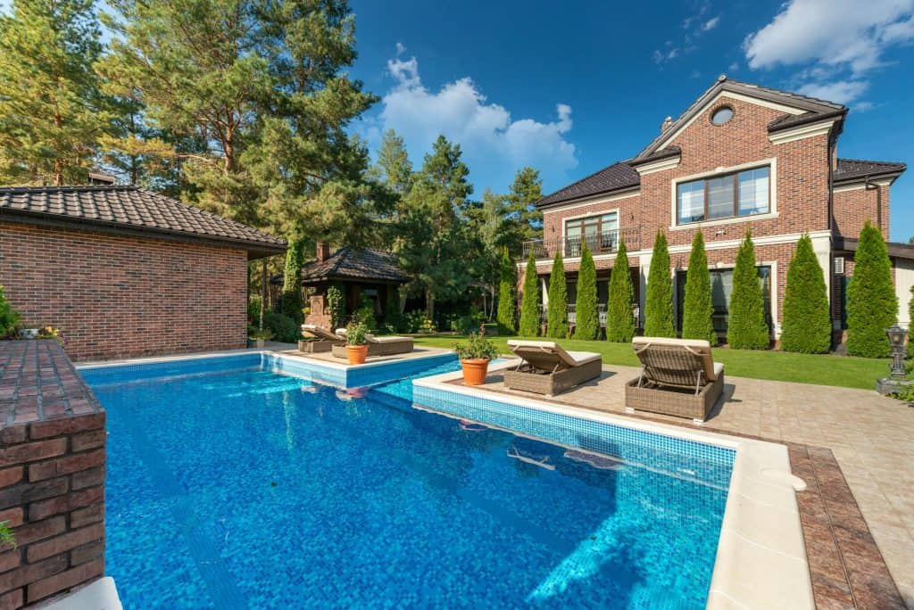 Beautiful backyard pool with clear blue water, surrounded by lush greenery and outdoor furniture, in a spacious residential yard.