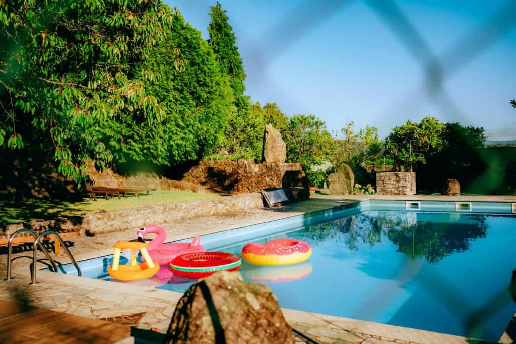 Beautiful backyard pool featuring colorful floaties, surrounded by lush greenery and natural rock accents, perfect for relaxing and enjoying warm weather.