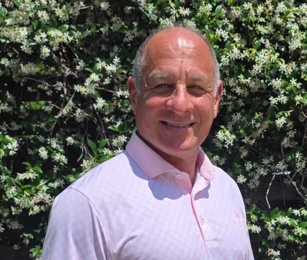 An experienced builder standing outdoors in front of a lush, flowering shrub, showcasing the company's dedication to quality craftsmanship and customer satisfaction.