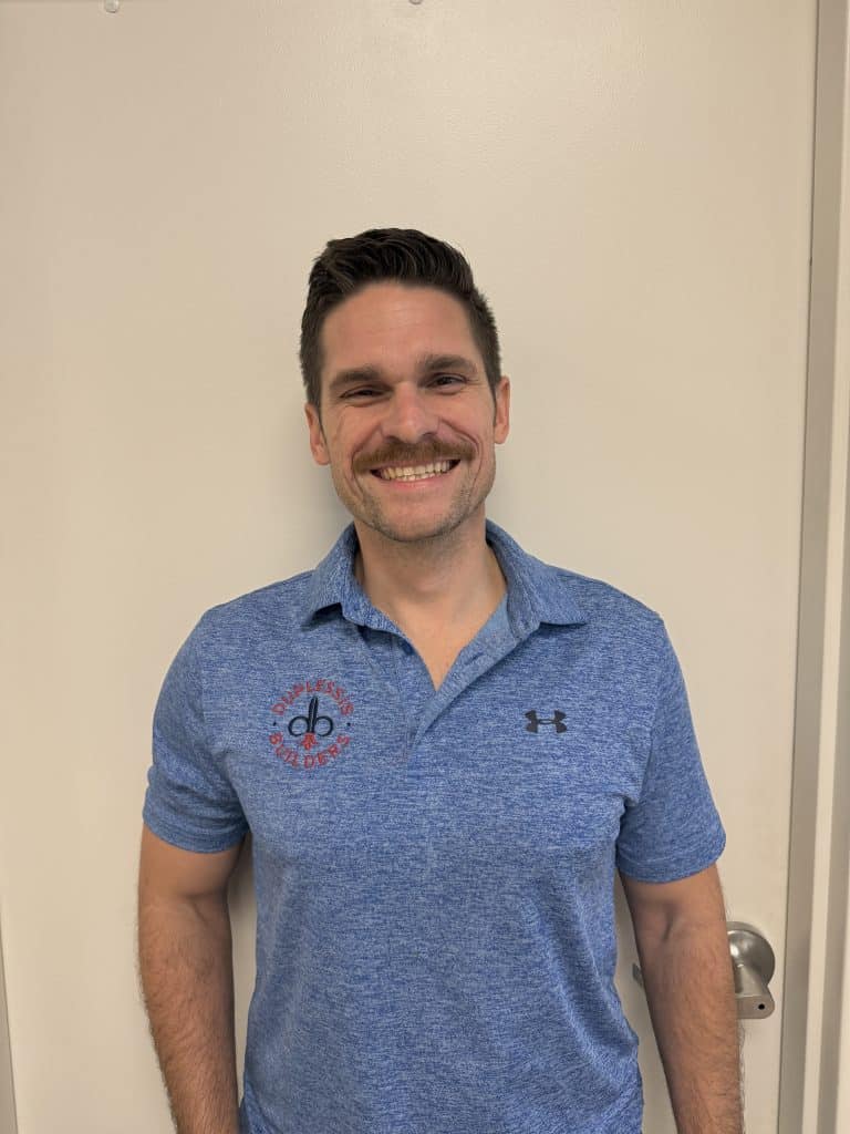 An image of a smiling man in a blue polo shirt with Duplessis Builders logo, standing against a plain wall, representing the friendly and professional team behind the company.