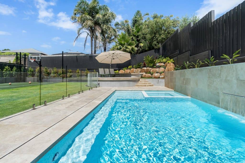 Modern backyard pool with sports court, lush landscaping, and outdoor seating area, perfect for family fun and entertaining guests.