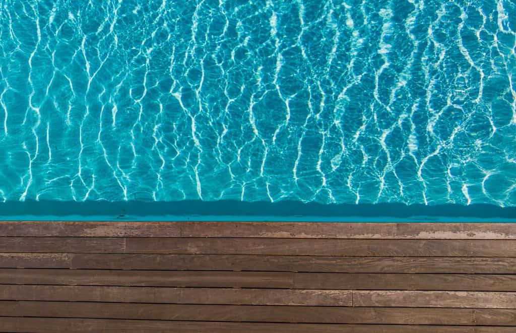 A clear view of a fiberglass pool surface with shimmering water, adjacent to a wooden pool deck, illustrating the quality of fiberglass pool installations.