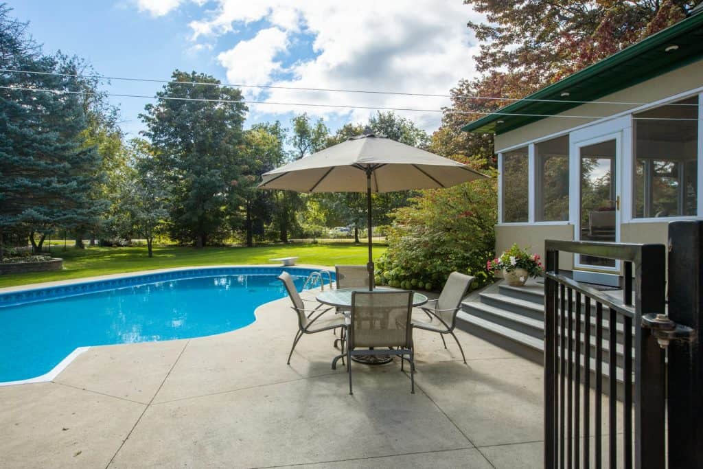 A beautiful outdoor pool area featuring a spacious patio with a table, chairs, and umbrella, perfect for relaxing and entertaining in a backyard makeover.