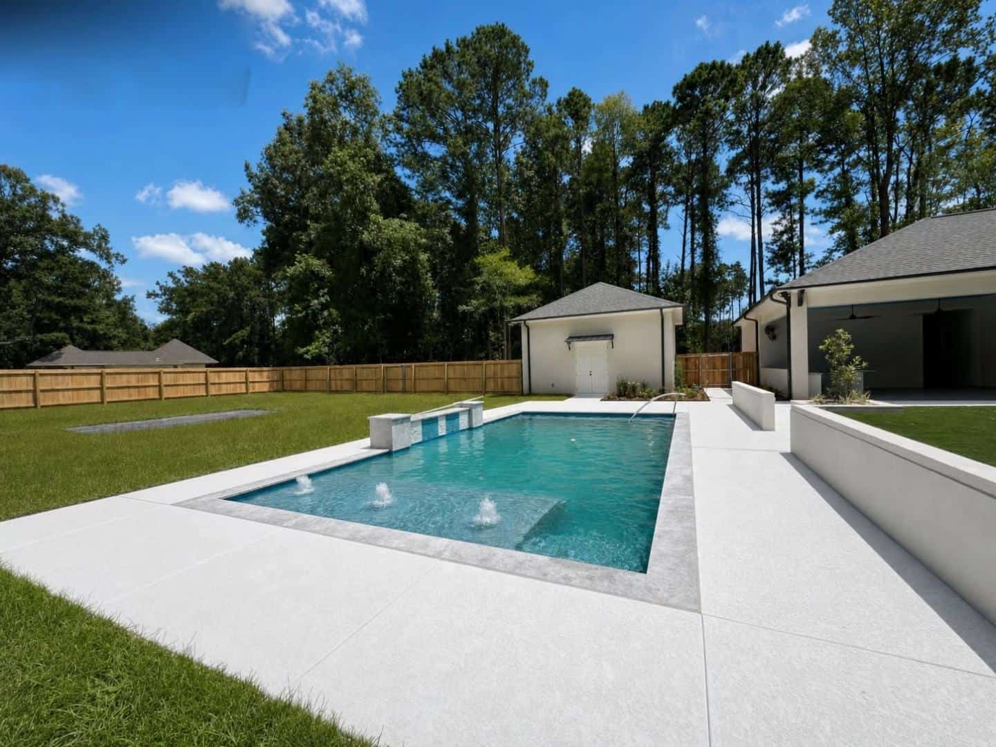 Gunite pool with deck jets, raised planters, and travertine decking in Baton Rouge