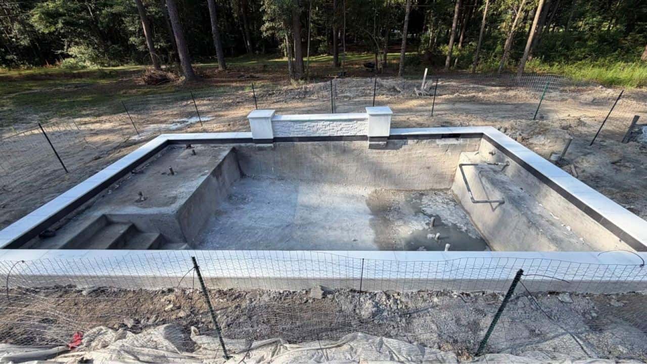 Gunite pool shell under construction with temporary safety fence around the excavation