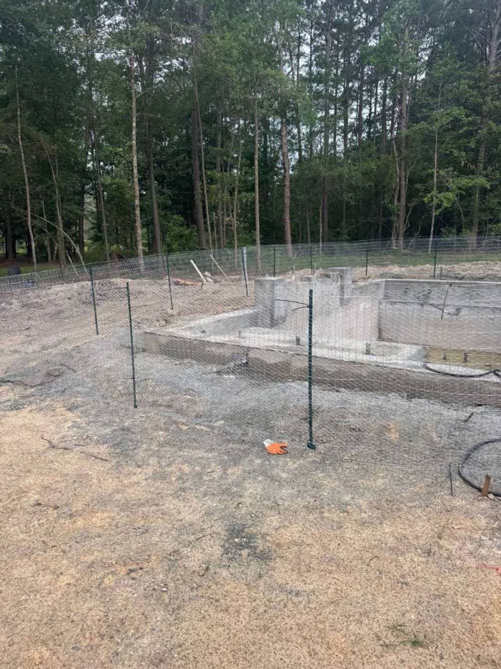 Freshly shot gunite pool shell with temporary safety fence at a Baton Rouge job site